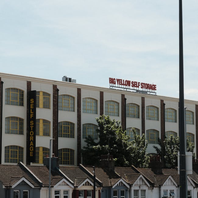 The image shows a multi-storey building with a sign on the roof indicating 'Big Yellow Self Storage' in red letters. The building's facade features large yellow-framed windows with a white exterior ac